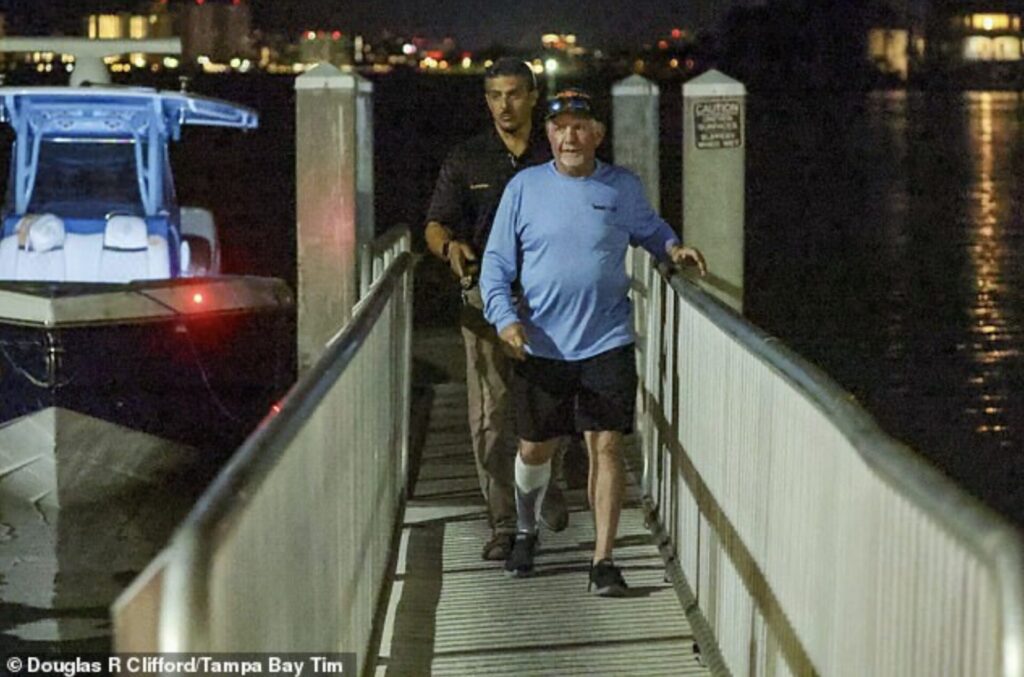 effry Knight, in a blue shirt and cap, is escorted by an investigator on a dock at Clearwater Harbor, Florida, at night after the fatal Clearwater Ferry crash, with a boat docked in the background
